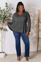 Plus size woman modeling long sleeve tiered tunic top with blue jeans in casual indoor setting