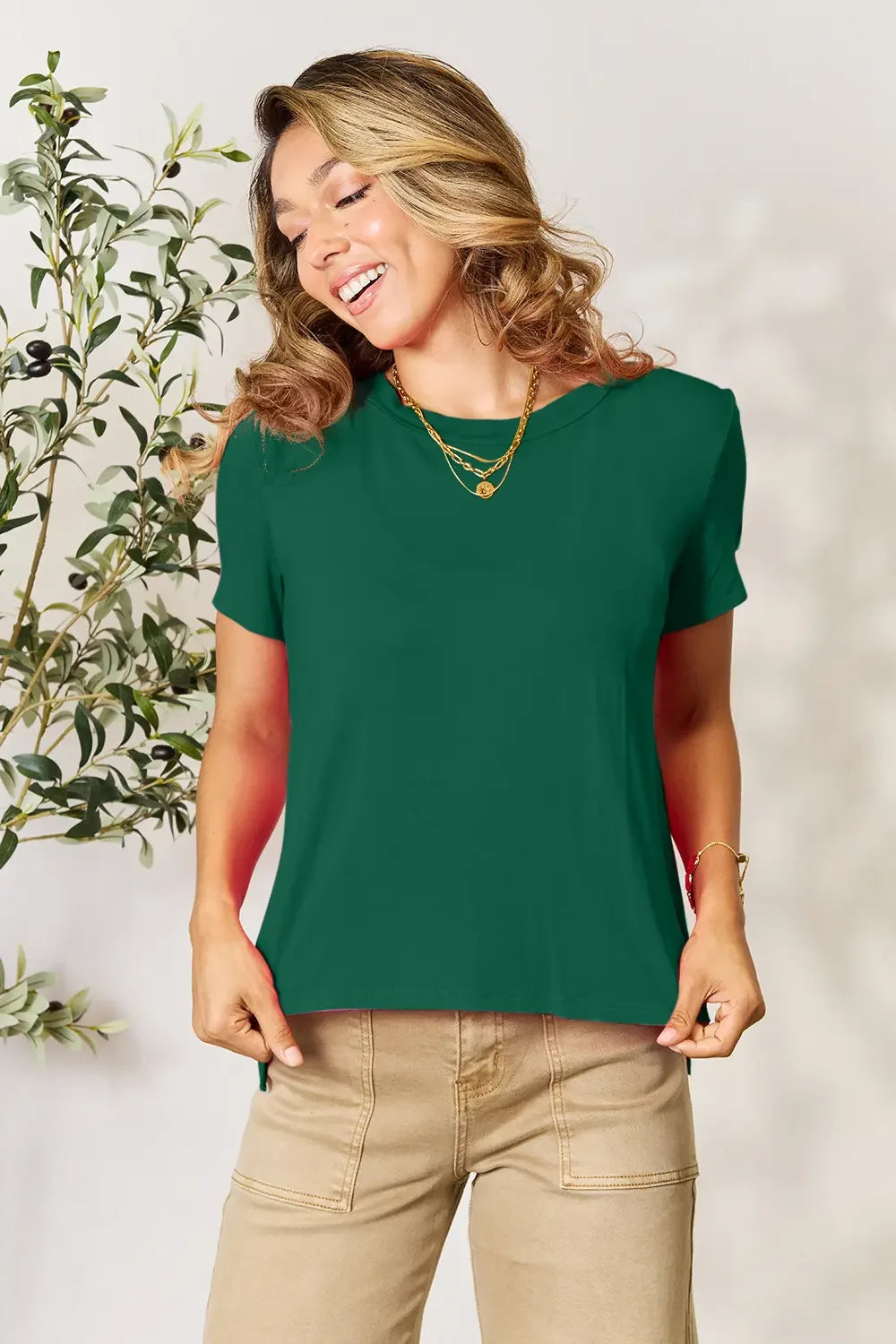 Woman in green short sleeve top with gold necklaces and beige pants, casual fashion style
