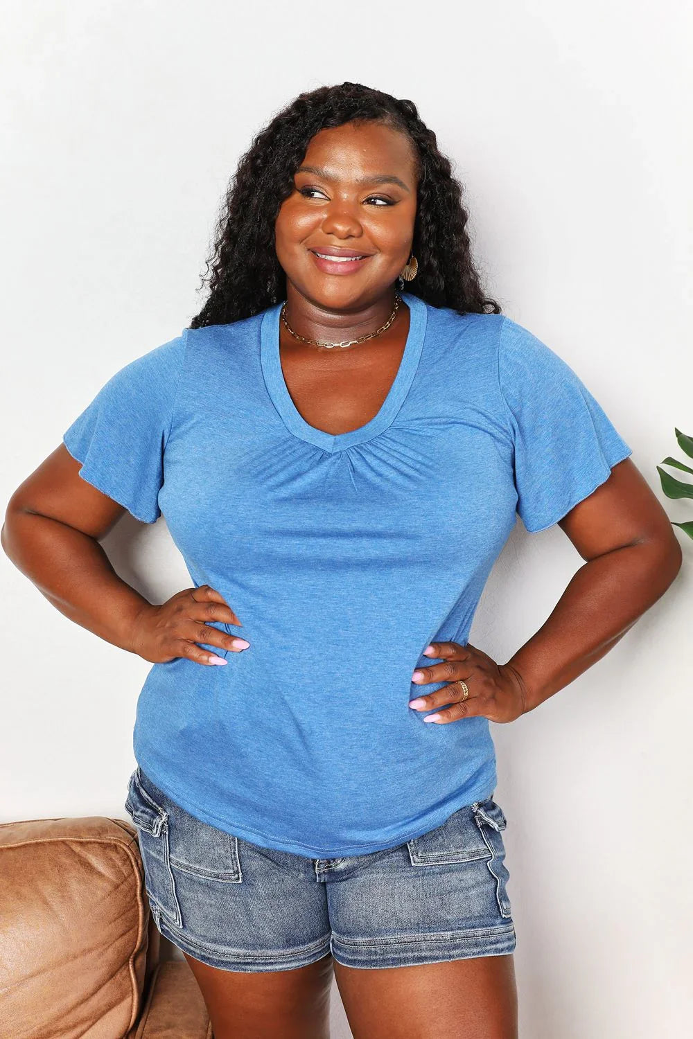 Woman in casual blue V-neck T-shirt and denim shorts, standing indoors and smiling