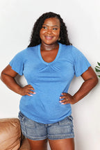 Woman in casual blue V-neck T-shirt and denim shorts, standing indoors and smiling