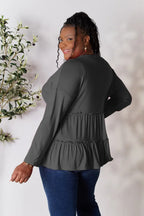 Plus size woman in long sleeve ruffle peplum top and blue jeans standing near plant