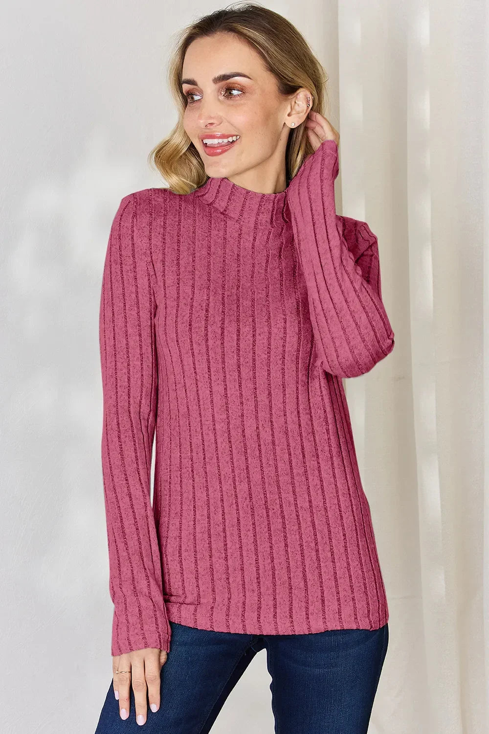 Woman wearing a pink ribbed long sleeve mock neck sweater with blue jeans