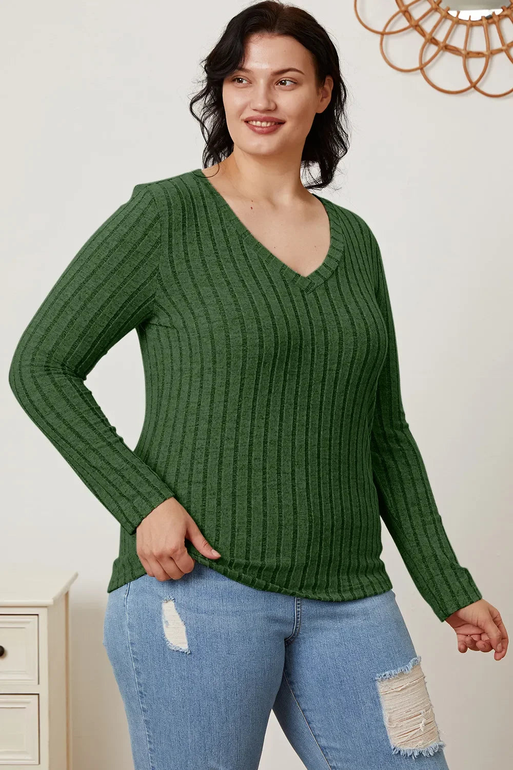 Woman wearing a green ribbed V-neck long sleeve top and ripped blue jeans