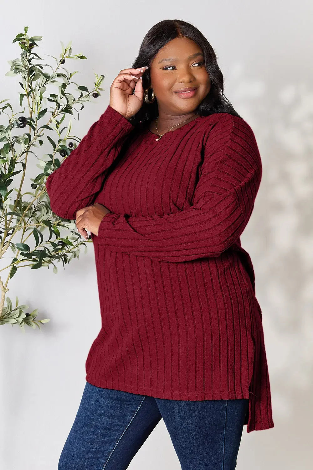Woman in a long-sleeve ribbed burgundy sweater and blue jeans posing indoors