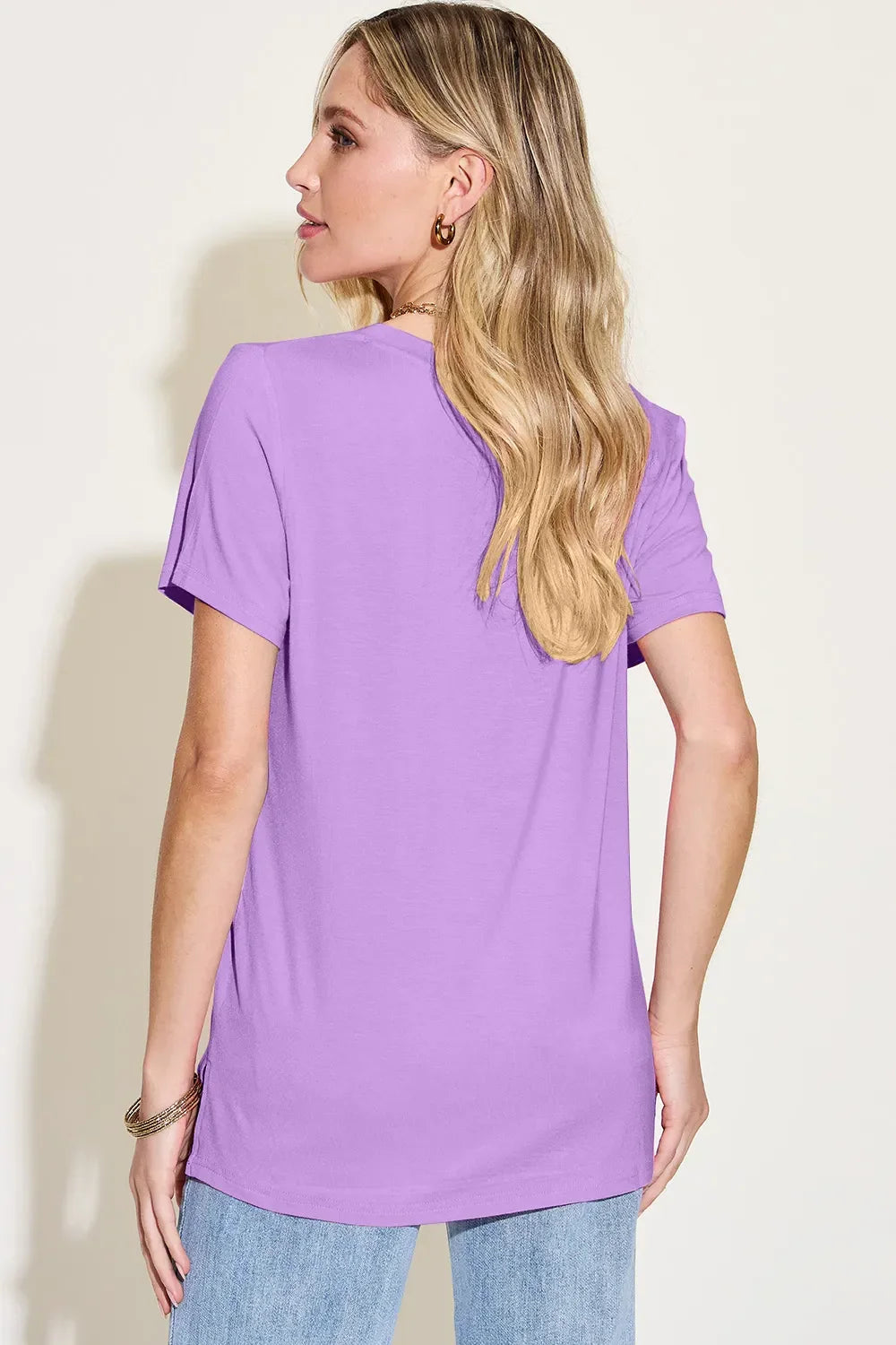 Woman wearing a lavender short sleeve t-shirt and light blue jeans, back view