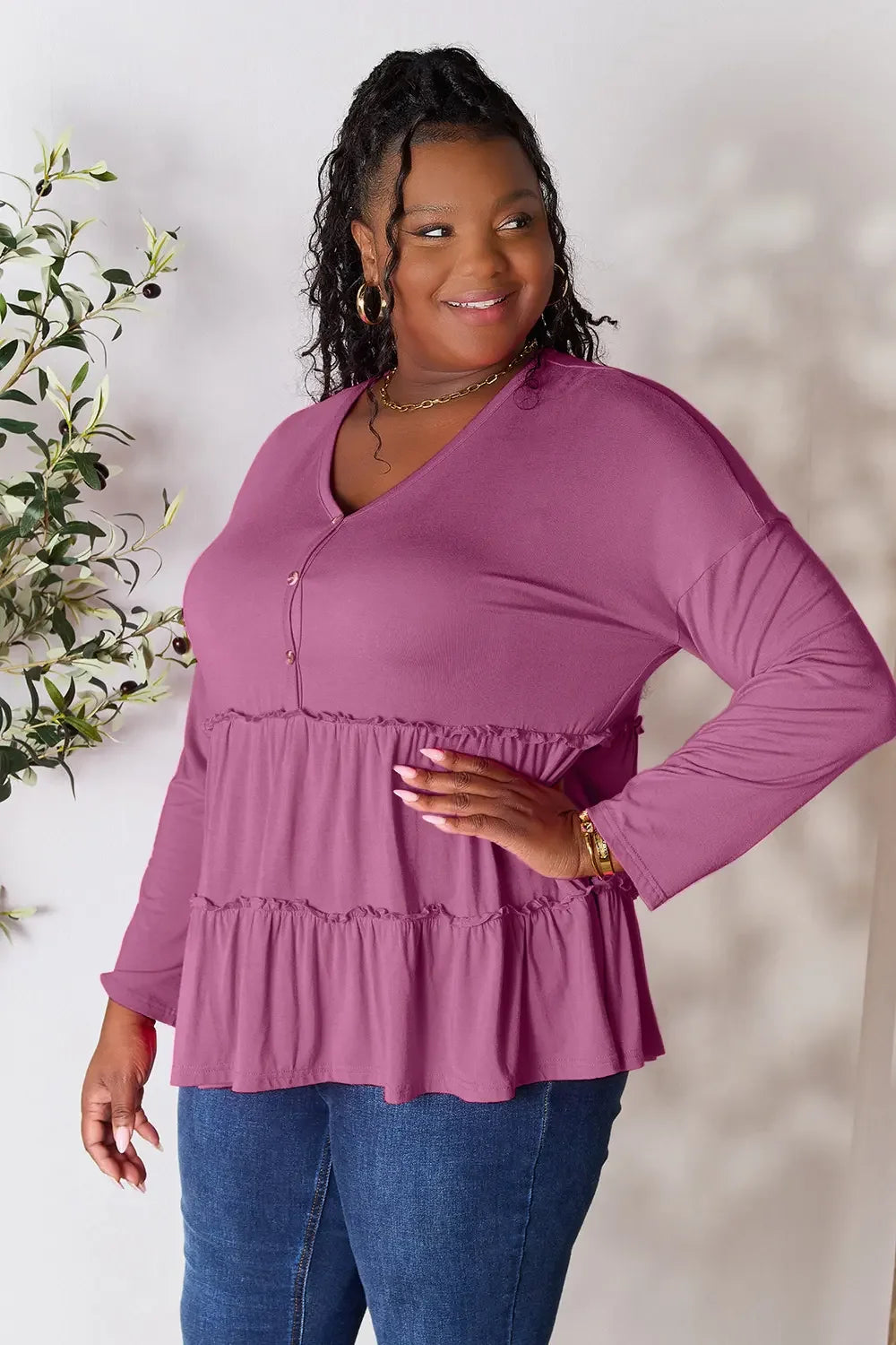 Smiling woman wearing a mauve tiered long sleeve blouse with V-neck and blue jeans