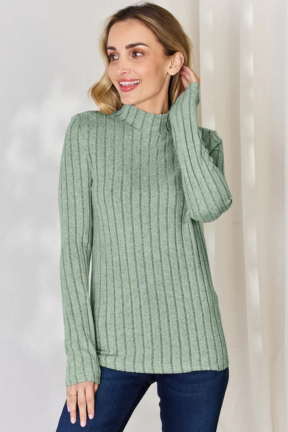 Woman wearing a sage green ribbed knit long sleeve sweater with mock neck